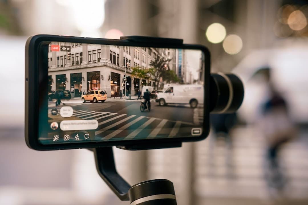A smartphone on a gimbal stabilizer filming a city street.