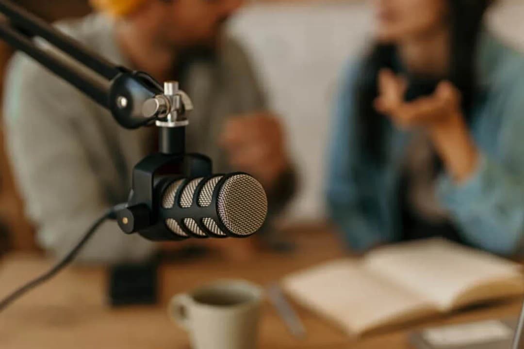 A studio podcast microphone with two people in conversation.