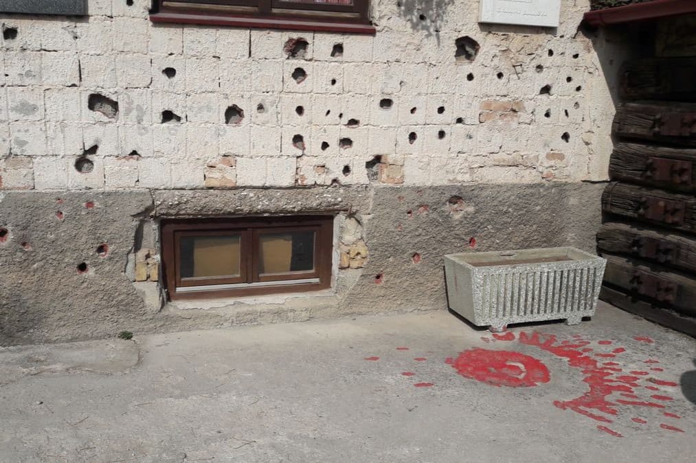 A Sarajevo Rose: a mortar-shell scar in the pavement filled with red resin, beside a wall still pocked with shrapnel from the siege.